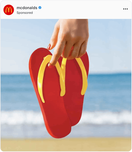Hands holding red and yellow flip flops at the beach