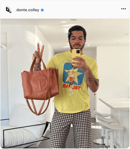 Influencer Donte Colley takes selfie in front of mirror. holding handbag and making the peace sign with his right hand