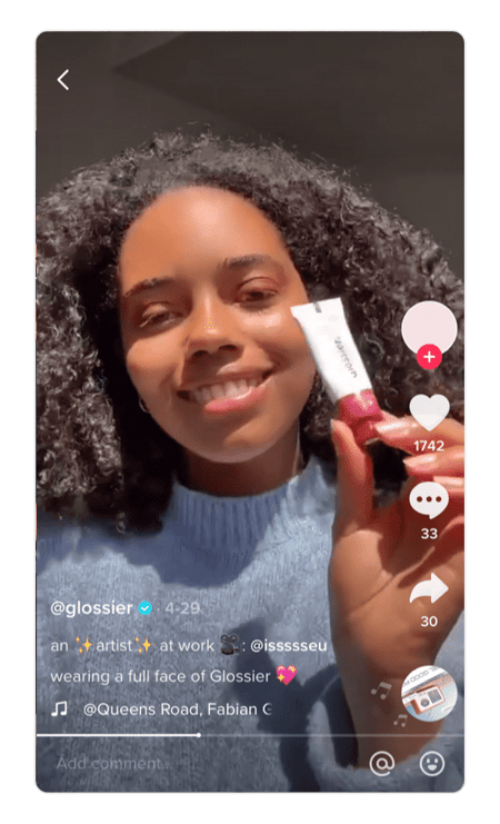 Screenshot of TikTok by Glossier. Woman holds product in front of camera and smiles.