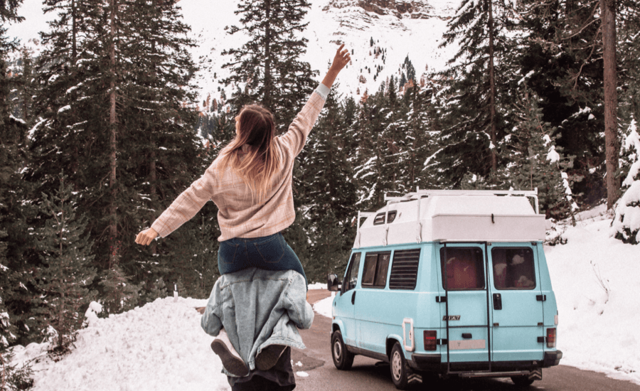 Person on someone's shoulders with a snowy mountain and blue van in the background