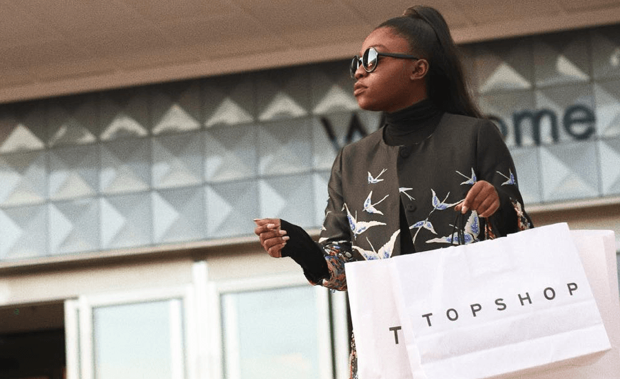 Woman wearing sunglasses looking while holding shopping bags in front of a shopping centre