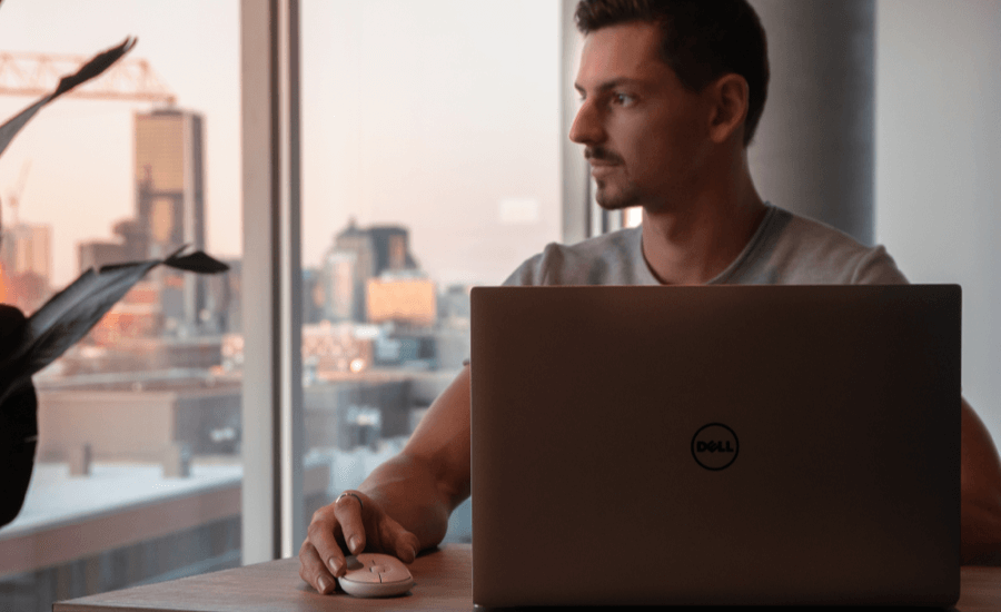 Man working on laptop looks outside a window at sunset