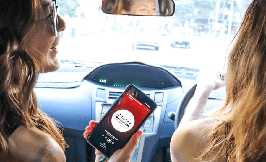 Two people in a car smiling at each other with a phone pointed at the camera