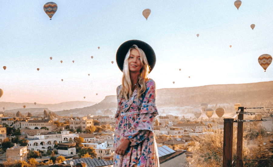Woman wearing a hat stands in front of air balloons with a scenic backdrop