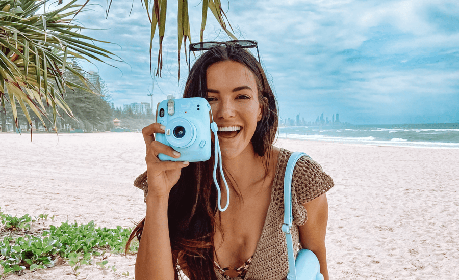 Woman at the beach smiles at the camera with a camera in hand