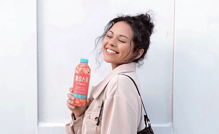 Woman holding a bottle smiles with her eyes closed on a white background