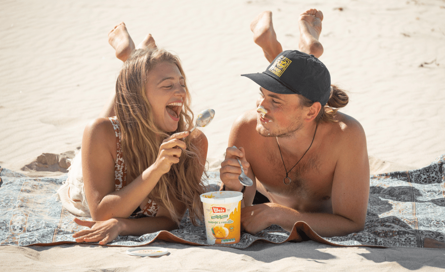 Two people lie on a beach towel eating ice cream