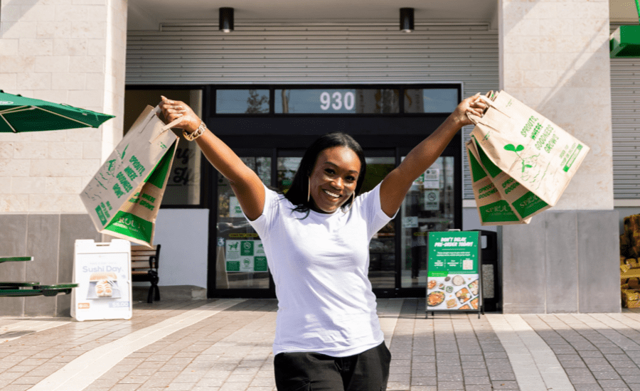 Woman smiles at camera holding one shopping bag in each hand high in the air
