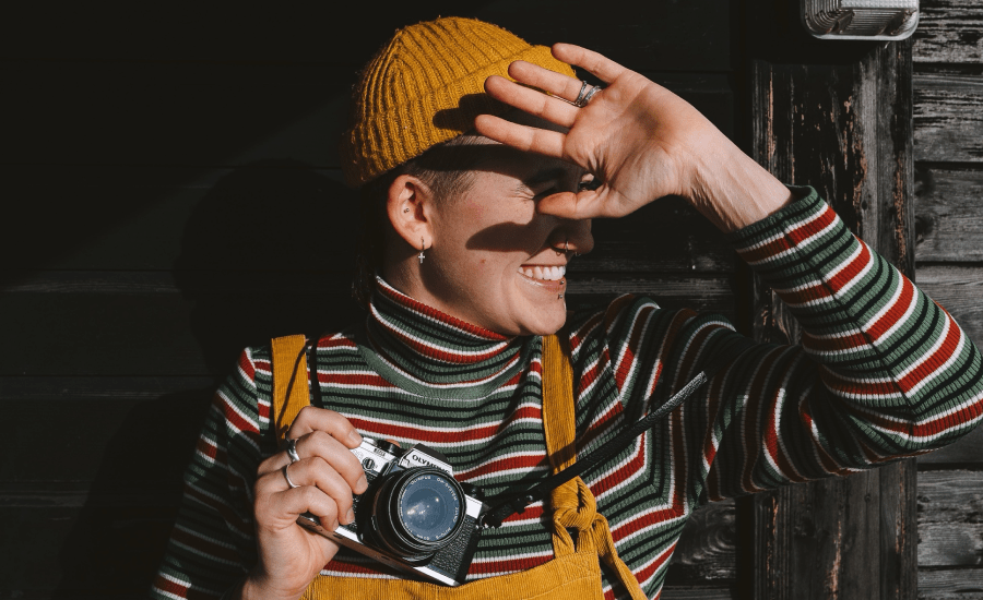 woman shades her face from sunlight while holding a camera