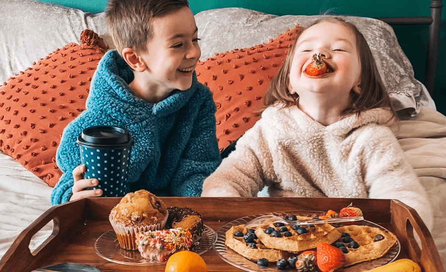 Two children laughing and enjoying a breakfast in bed