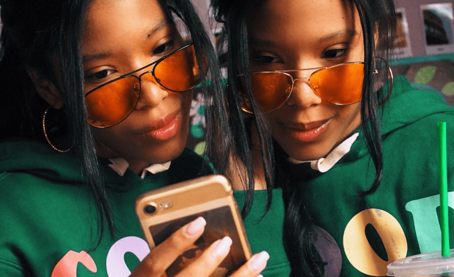 Two women look at phone screen with orange sunglasses on