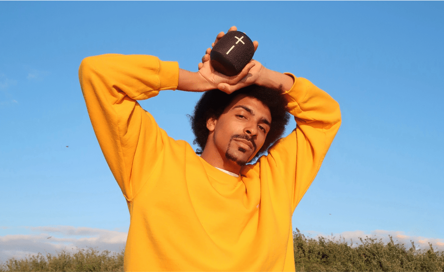 Man in yellow jumper holds a speaker above his head