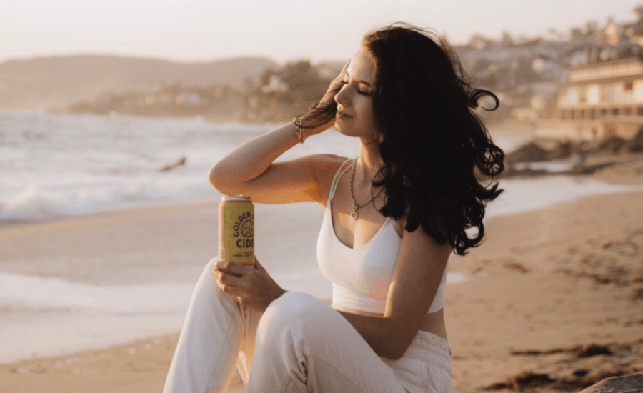 woman sits on the beach holding a can