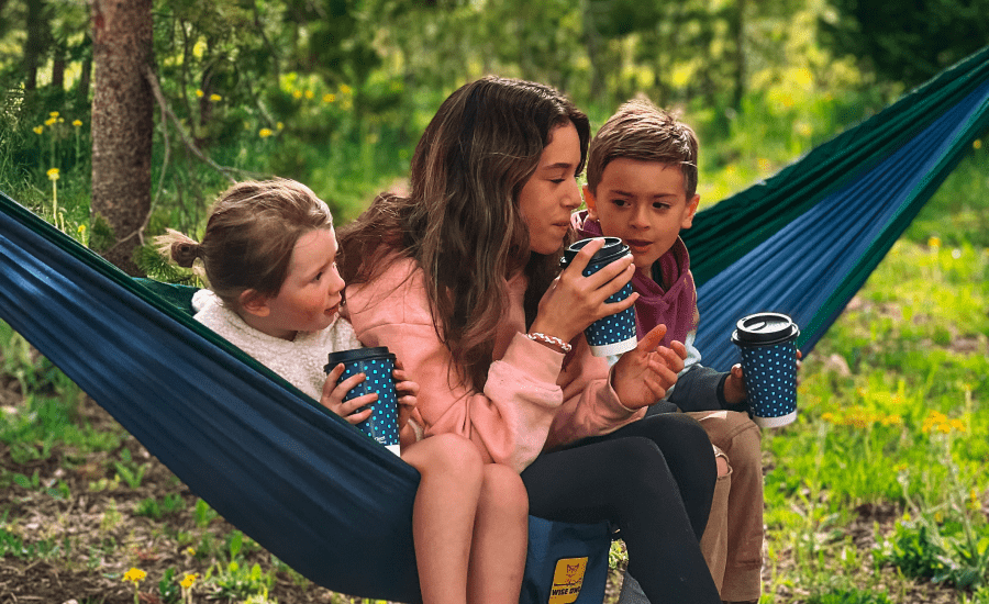 mother and kids drinking out of cups on a hammock
