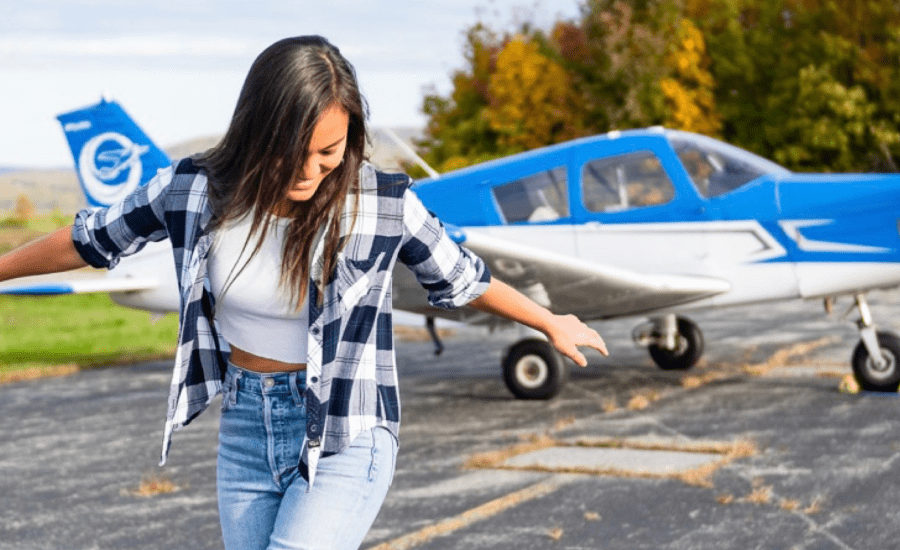 woman stands in front of a small plane looking downwards with arms outstretched