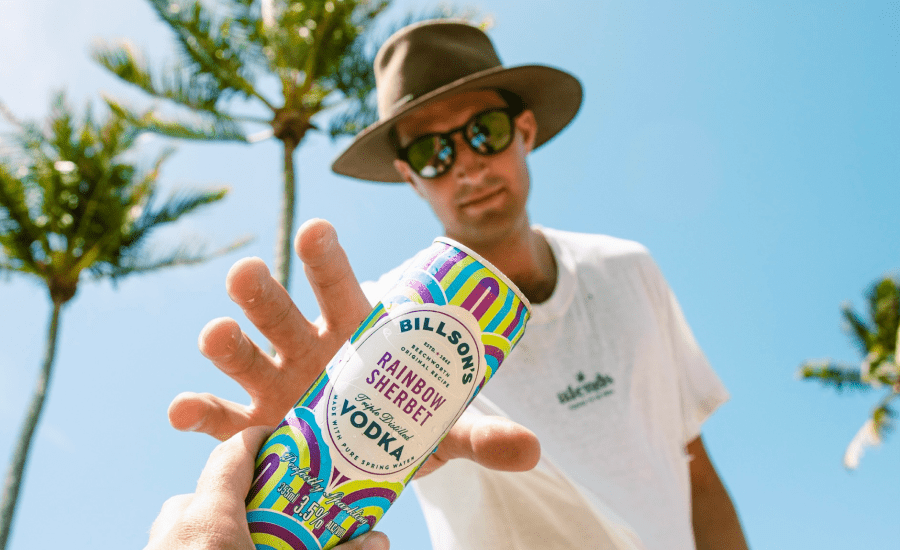 man in a hat reaches towards the camera for a canned drink