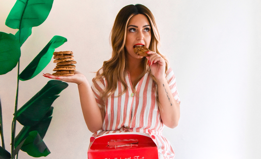 a girl holding a pile of cookies takes a bite of one