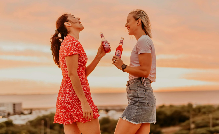 Two female creators enjoying a drink together in front of a beautiful sunset