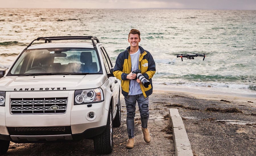TRIBE creator @jb holding a camera in front of his Range Rover in front of the ocean